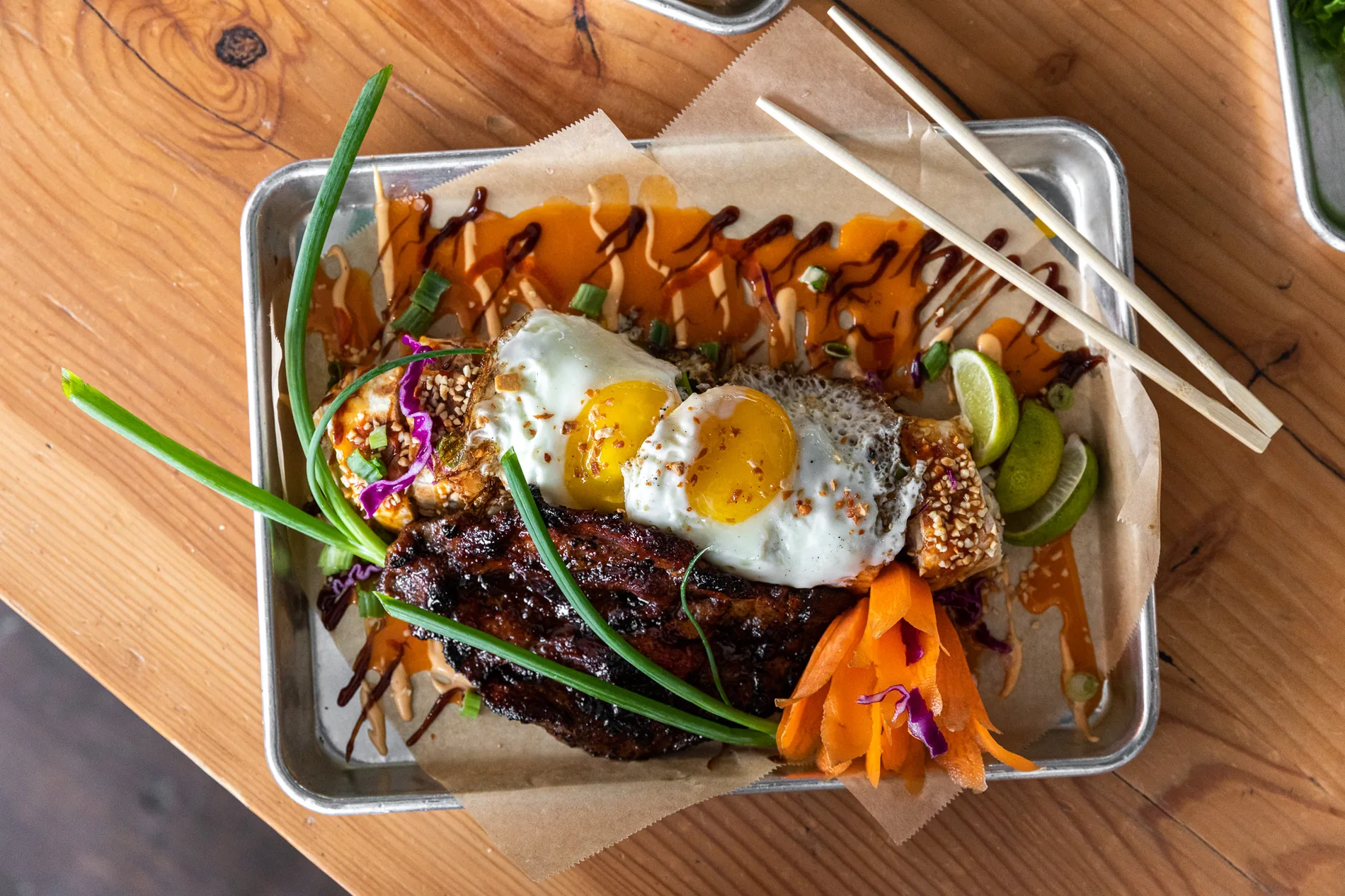 Grilled Thai pork with fried egg, chili and lime on a metal tray