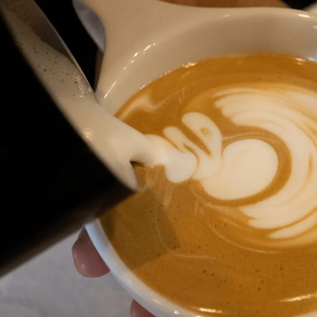 A barista pours steamed milk into a latte at Bel Horizon Coffee 606, forming heart latte art.